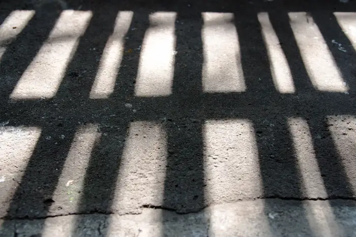 A stock image of shadow of prison bars on a cement ground
